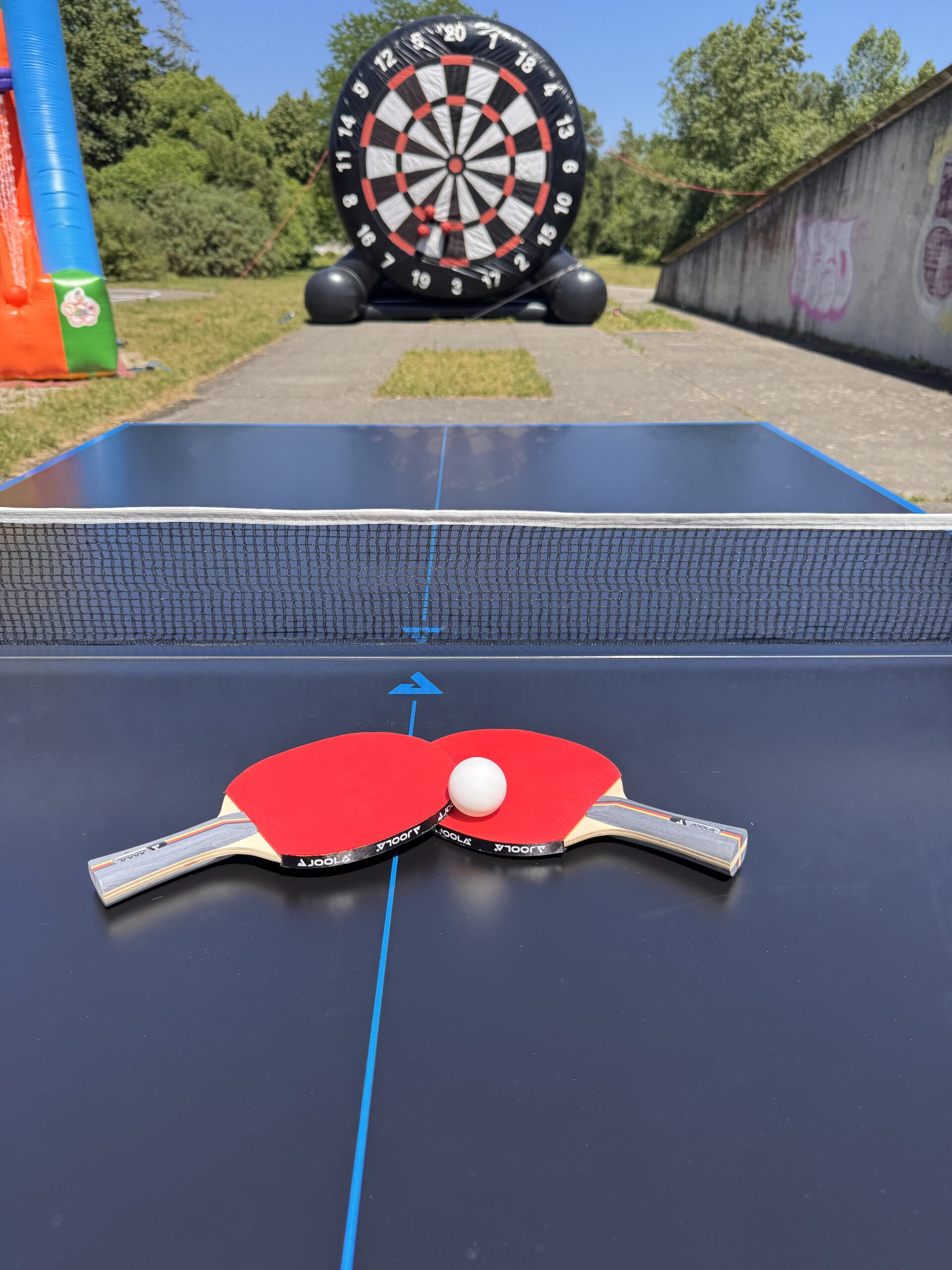 Zwei Tischtennisschläger und Ball auf einer Tischtennisplatte im Outdoor-Bereich